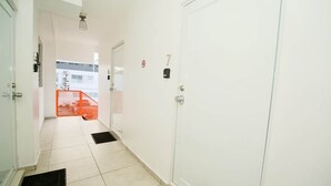 A hallway with white walls, a door marked with the number 7, and a red safety railing in the background. - 1.5• Generator • 2nd Floor • Parking • 1BR • 396sf (Mayagüez)