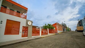 A street view with buildings, a clock, and a parked truck. - 1.5• Generator • 2nd Floor • Parking • 1BR • 396sf (Mayagüez)