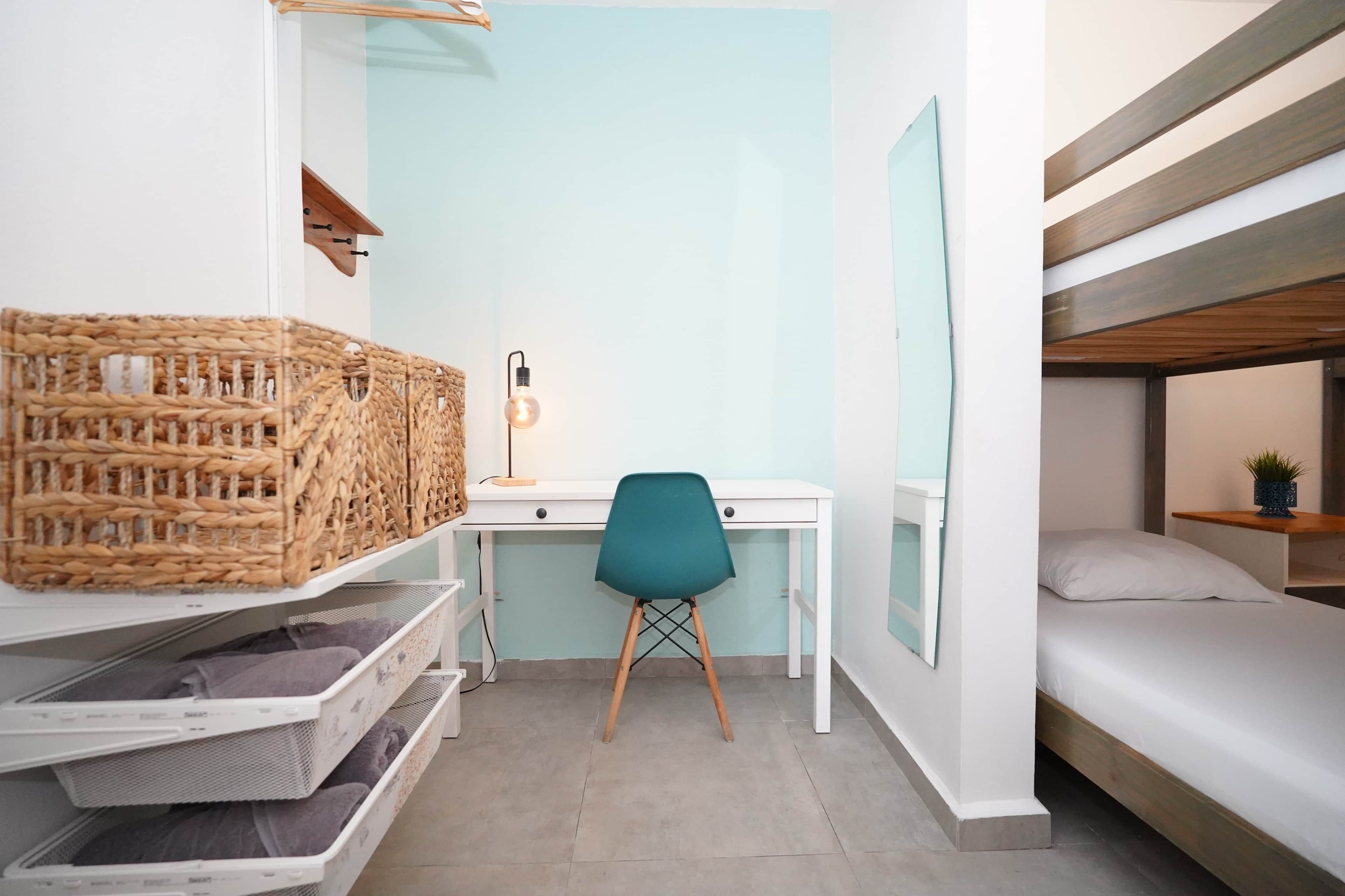 A compact room with a bunk bed, a desk with a chair, and storage shelves.