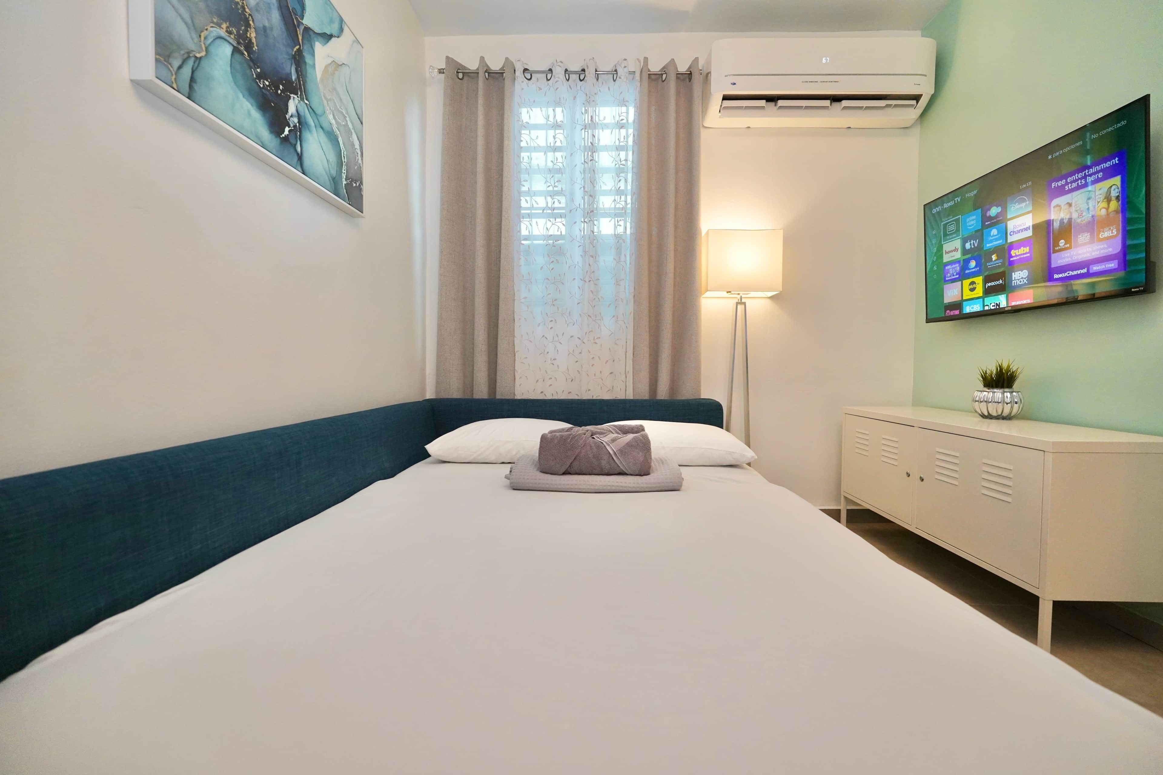 Habitación de hotel con cama, escritorio, televisor y ventana con cortinas.