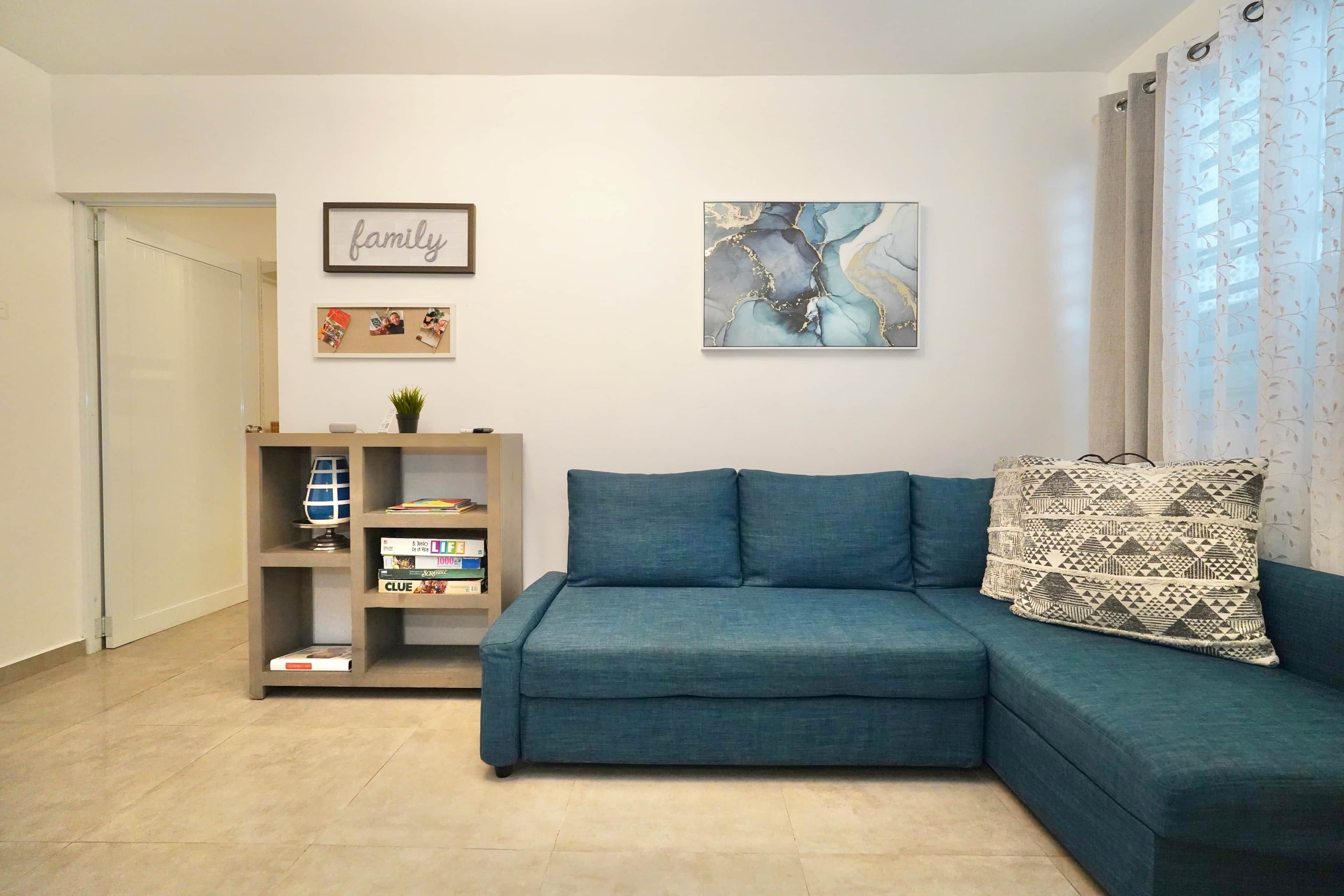 A living room with a teal sofa, a bookshelf, a framed 'family' sign, and abstract art on the wall.