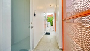 A hallway with a door, a wall-mounted light fixture, and a tiled floor. - 1.5• Generator • 2nd Floor • Parking • 1BR • 396sf (Mayagüez)