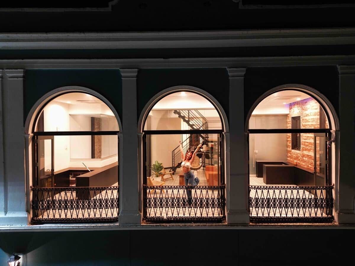 Tres ventanas arqueadas con barandilla de metal, una escalera y una habitación con cama y planta.