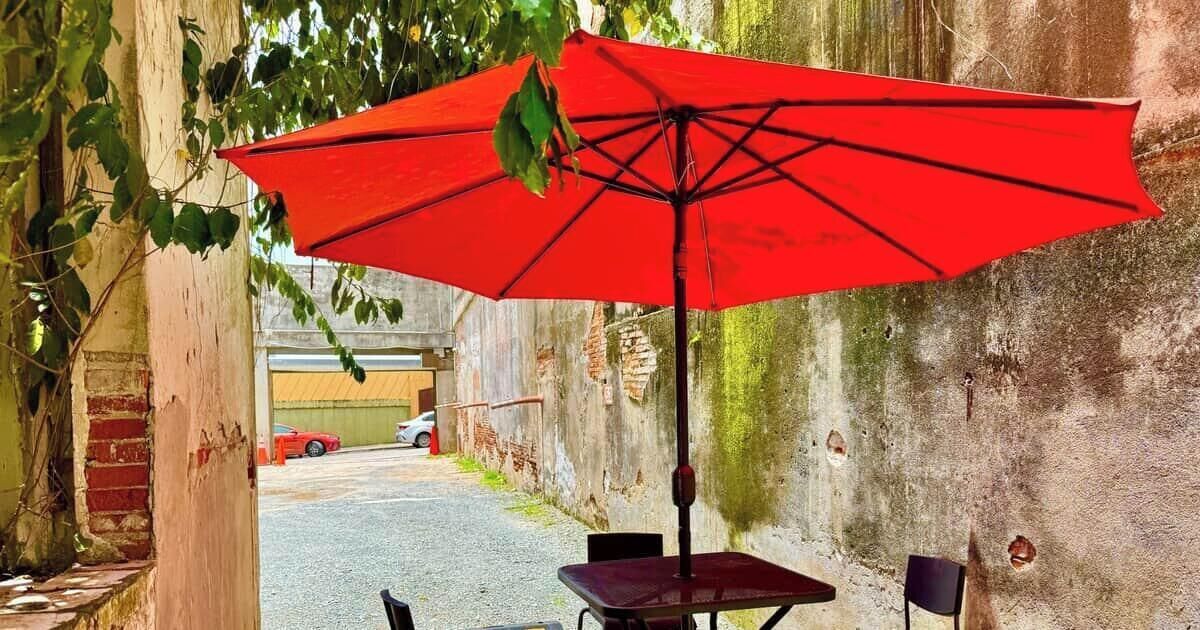 An outdoor seating area with a red umbrella, a brick wall, and a car in the background.