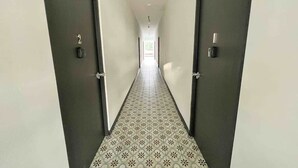 A corridor with patterned floor tiles, two doors on either side, and a light source at the end. - 5.2 Loft • Lobby • Generator • Parking • 2nd Floor (Mayagüez)
