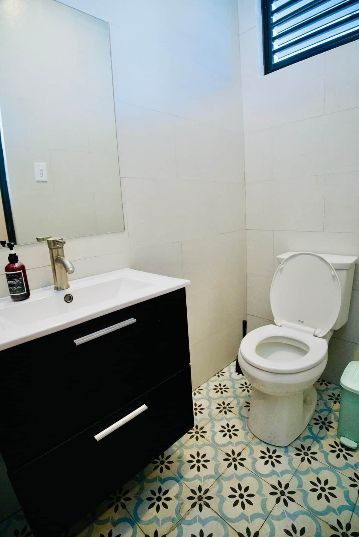 Et badeværelse med en hvid vask, et sort skab og et toilet med et blå mønstret gulv.