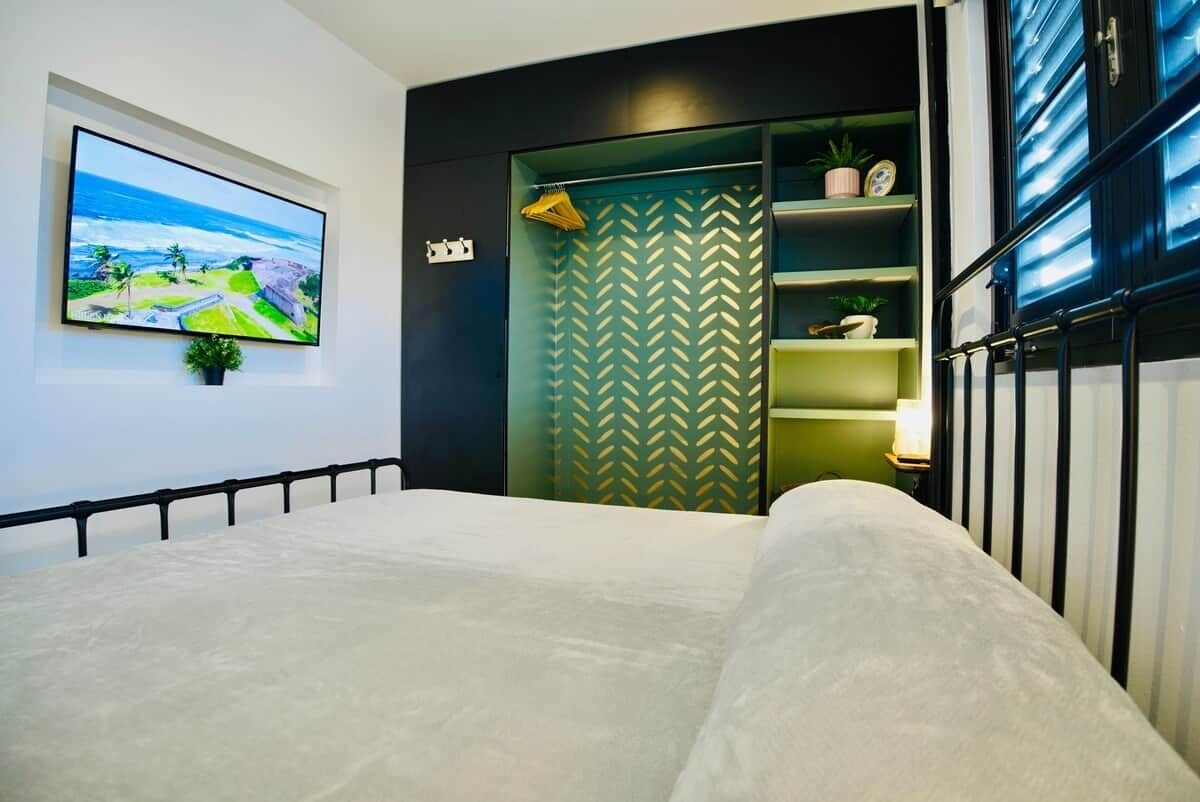 A bedroom with a bed, a television mounted on the wall, and a wardrobe with a herringbone pattern.
