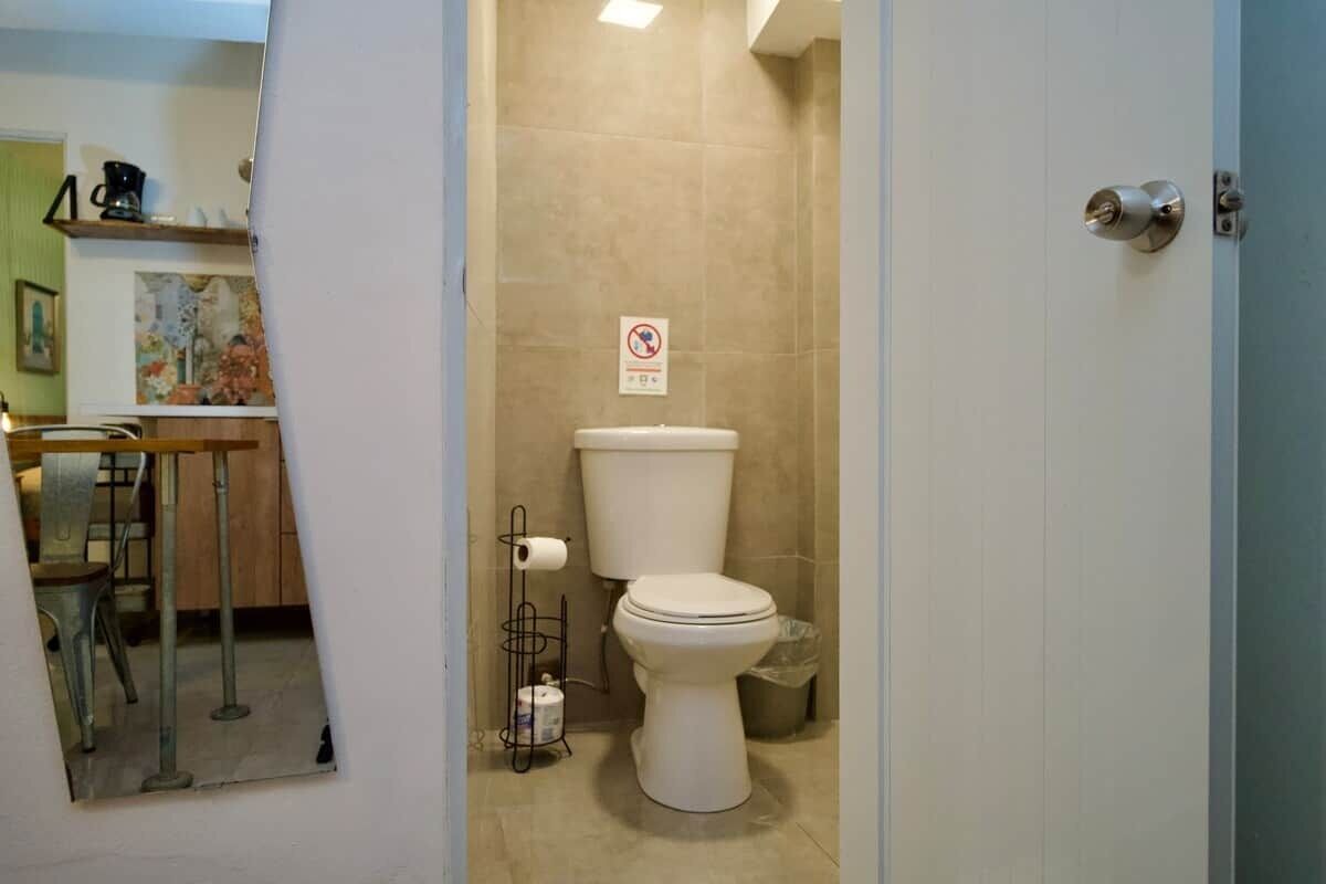 A bathroom with a toilet, a trash bin, a paper towel holder, and a no-smoking sign.