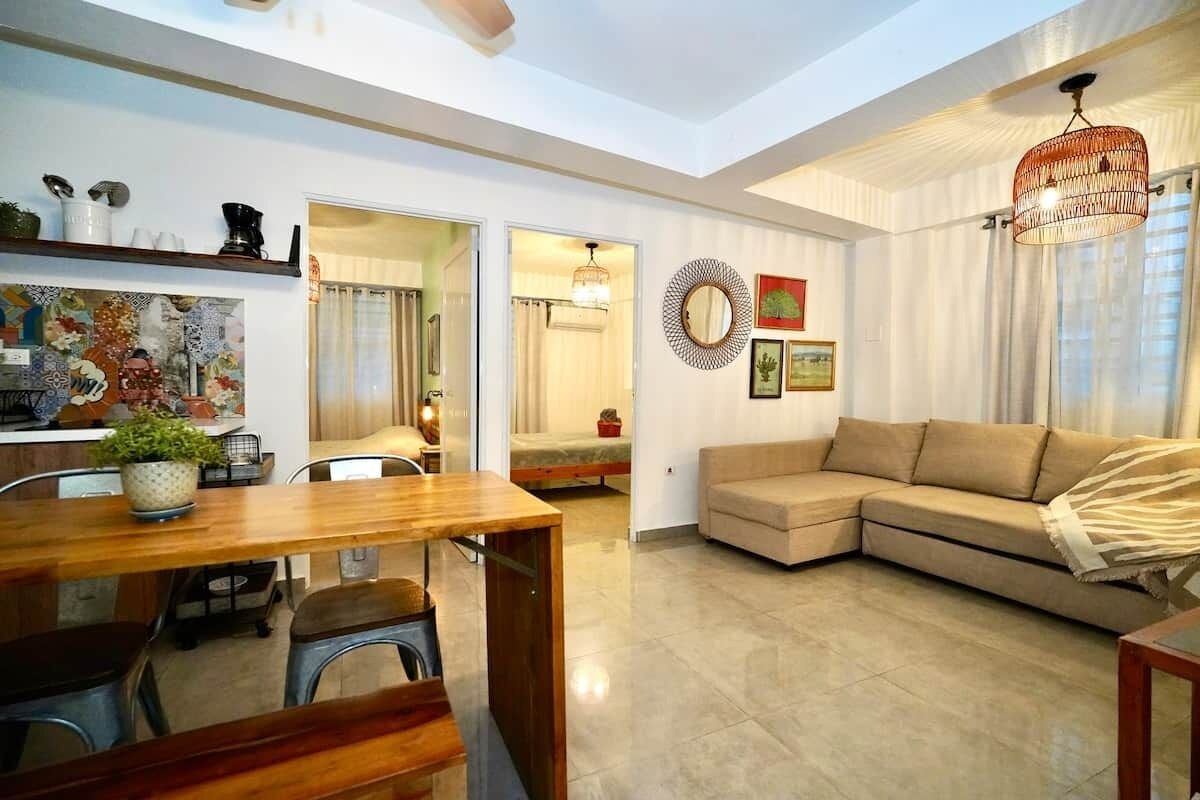 A modern living room with a wooden dining table, a sofa, and a kitchen area with a countertop and cabinets.