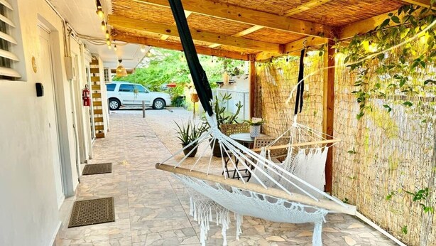 A covered outdoor area with a hammock, a wall with climbing plants, and a white car in the background. - 3.9 Near Beach • Generator • Hammock • 1st Floor (Miradero)