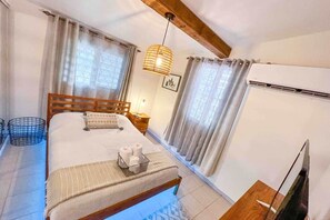 A bedroom with a bed, bedside tables, a hanging lamp, curtains, and an air conditioning unit.