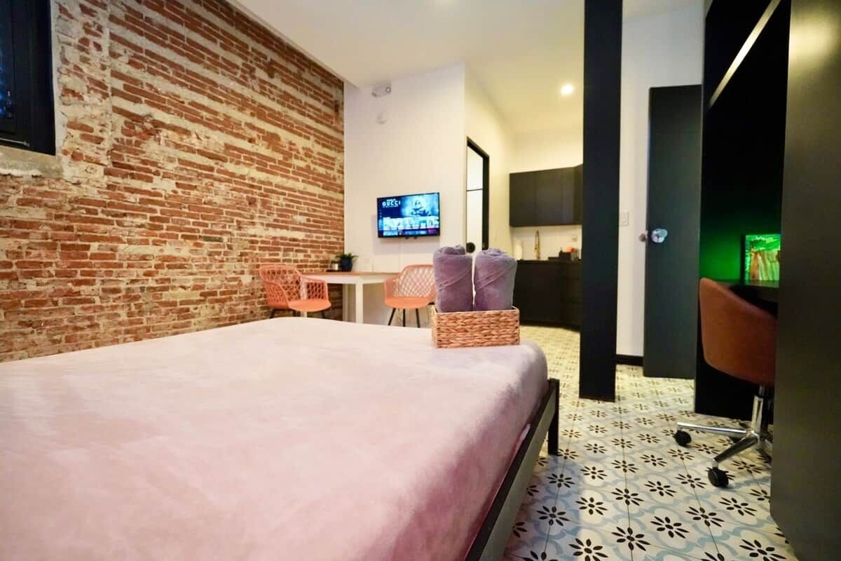 A hotel room with a brick wall, a bed, a TV, a desk, and a chair.