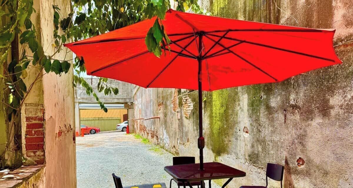 An outdoor seating area with a red umbrella, a brick wall, and a car in the background.