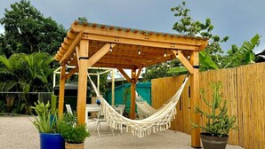 Une pergola en bois, agrémentée d’un hamac, de plantes en pot et d’un sol recouvert de gravier.