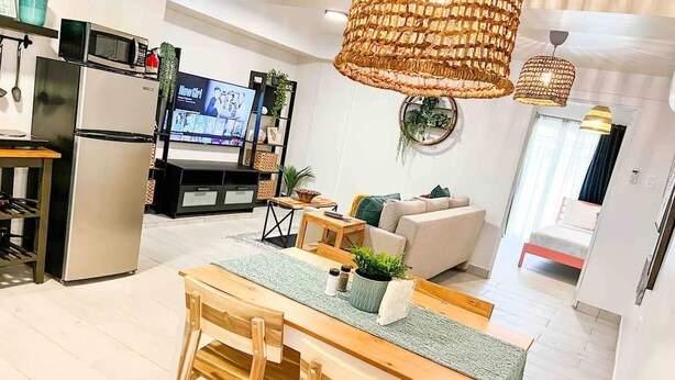 Une cuisine moderne équipée d’un réfrigérateur, d’un four à micro-ondes et d’une télévision. Un coin repas est aménagé avec une table et des chaises en bois.