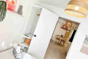 A room with a white door, a basket with bottles, a hanging plant, and a dining area with a table and chairs. - 3.2 Near Beach • Generator • Pergola • 2 Parkings (Miradero)