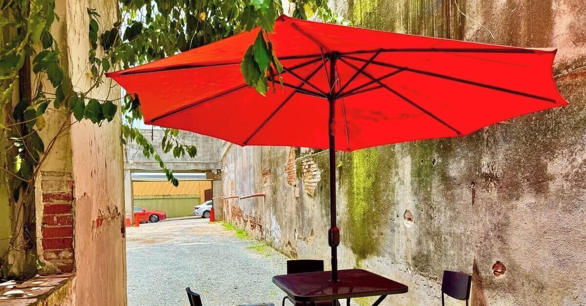 An outdoor seating area with a red umbrella, a brick wall, and a car in the background.