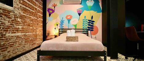 Una habitación con cama, pared de ladrillo, un mural colorido y baldosas de suelo estampadas.