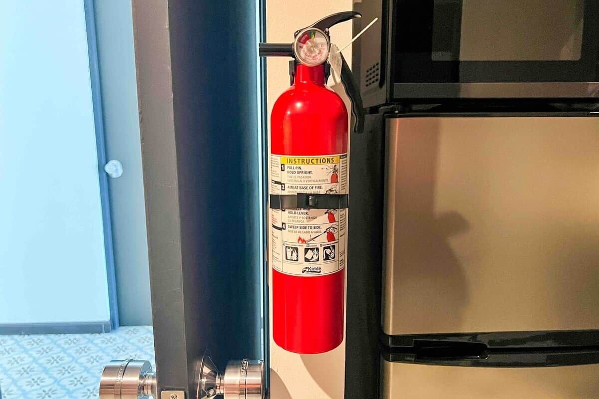 A red fire extinguisher mounted on a wall near a door and a stainless steel appliance.