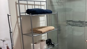 A bathroom with a white sink, a toilet, a glass shower enclosure, and a metal shelf with towels and toiletries. - Very Private Shared Room with Private Bathroom and Terrace (Ciudad de México)