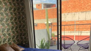 A bedroom with a bed, a chair, and a balcony with a view of buildings. - Very Private Shared Room with Private Bathroom and Terrace (Ciudad de México)
