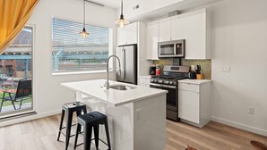 Een moderne keuken met witte kasten, een koelkast van roestvrij staal, een magnetron en een kookeiland met krukken.