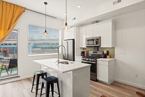 A modern kitchen with white cabinetry, a stainless steel refrigerator, a microwave, and an island with stools. - Fancy One Bedroom near Fishtown W/ private balcony. (Philadelphia)
