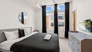 Een moderne hotelkamer met een bed, een ronde spiegel, een televisie en uitzicht op de stad.