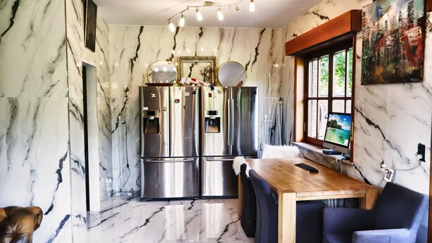 A kitchen with marble walls, stainless steel appliances, a wooden dining table, and a computer monitor.