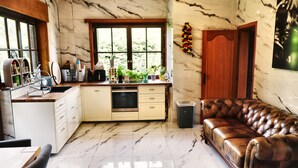 A kitchen with marble flooring, a wooden dining table, a leather sofa, and a trash bin.