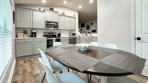 A modern kitchen with white cabinets, a microwave, and a dining table with chairs. - Beautiful 4-bedroom house with AC in Wimauma (Wimauma)