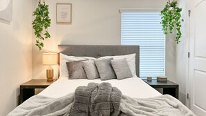 A neatly made bed with a grey blanket and pillows, a bedside lamp, and hanging plants. - Beautiful 4-bedroom house with AC in Wimauma (Wimauma)