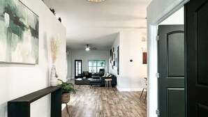 A hallway with a woven light fixture, a green patterned rug, a dark bench, and a dark door. - Beautiful 4-bedroom house with AC in Wimauma (Wimauma)