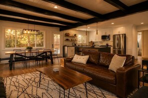 A modern kitchen with stainless steel appliances, a dining area with a wooden table and chairs, and a leather sofa with cushions. - Lake Arrowhead Mountain Hideaway by Navigate Stays (Lake Arrowhead)