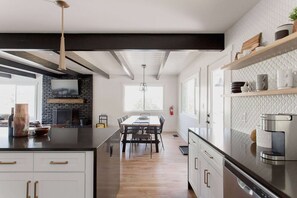 A modern kitchen with a central island, a dining area with a table and chairs, and a built-in fireplace. - Lake Arrowhead Mountain Hideaway by Navigate Stays (Lake Arrowhead)