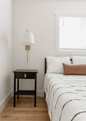 Un dormitorio con cama, mesita de noche, lámpara y ventana.