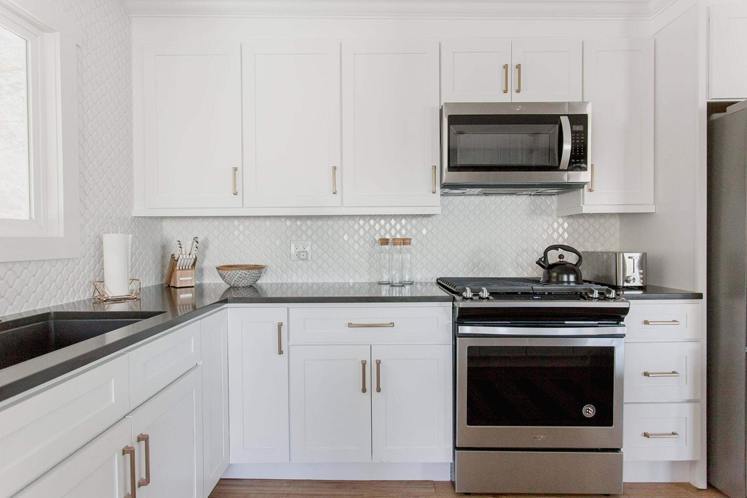 A modern kitchen with white cabinets, a stainless steel stove, a microwave, and a toaster.