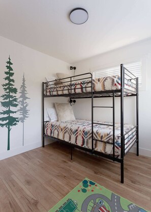 Ein Stockbett mit gemusterten Betttextilien, eine Wandsticker-Szene mit Bäumen und ein Teppich mit Sportmotiven.