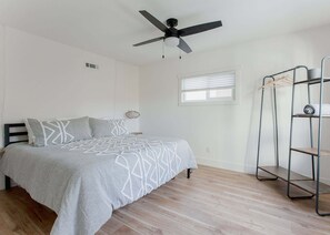 A bedroom with a bed, a ceiling fan, a window with blinds, and a metal shelf unit. - Lake Arrowhead Mountain Hideaway by Navigate Stays (Lake Arrowhead)
