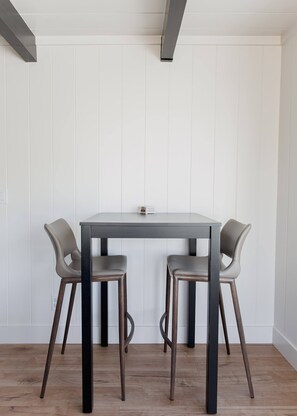 Una mesa de comedor con dos sillas, paredes blancas con paneles y piso de madera.
