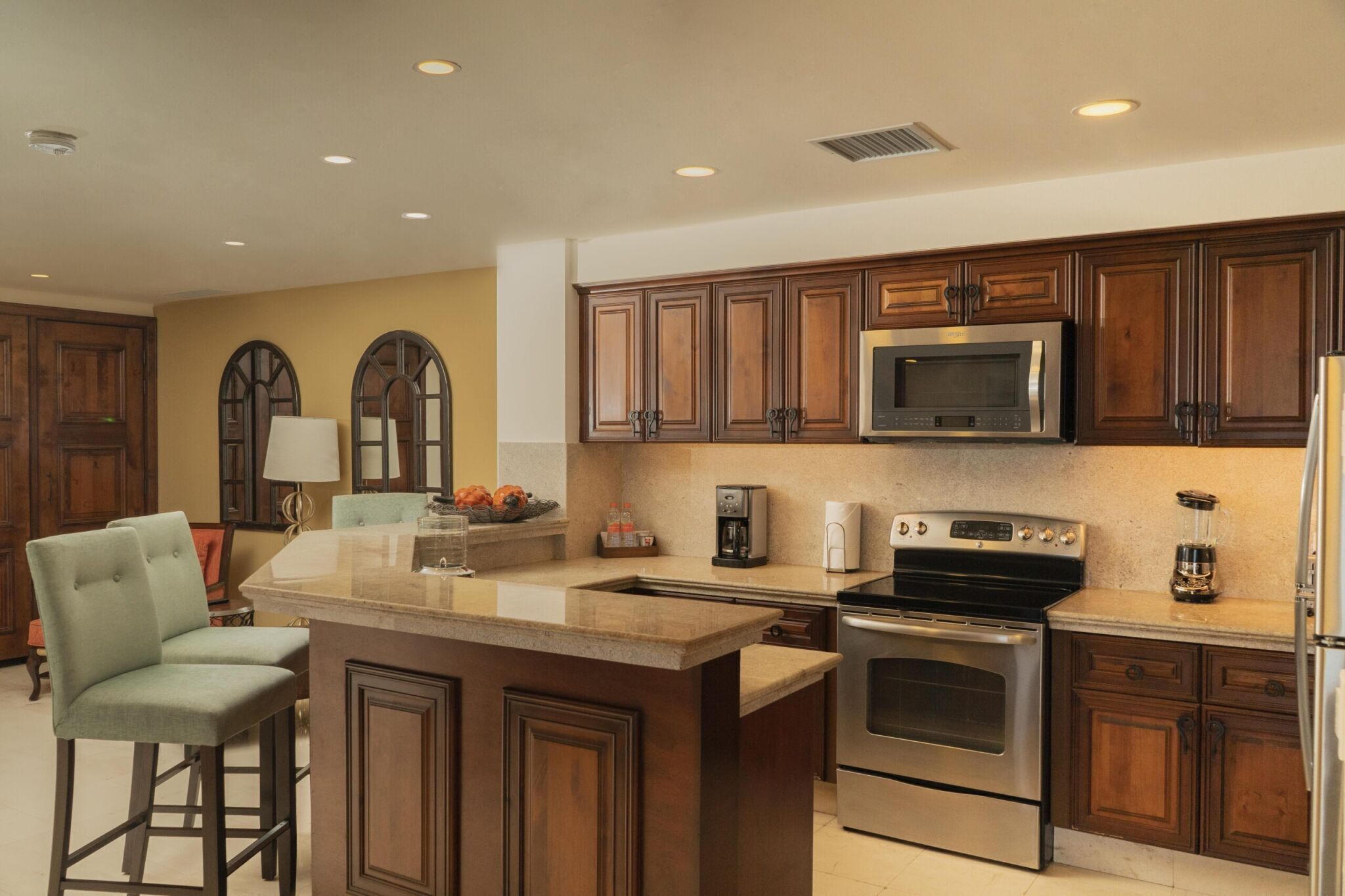 A kitchen with wooden cabinets, a stainless steel oven, a microwave, and a bar stool.