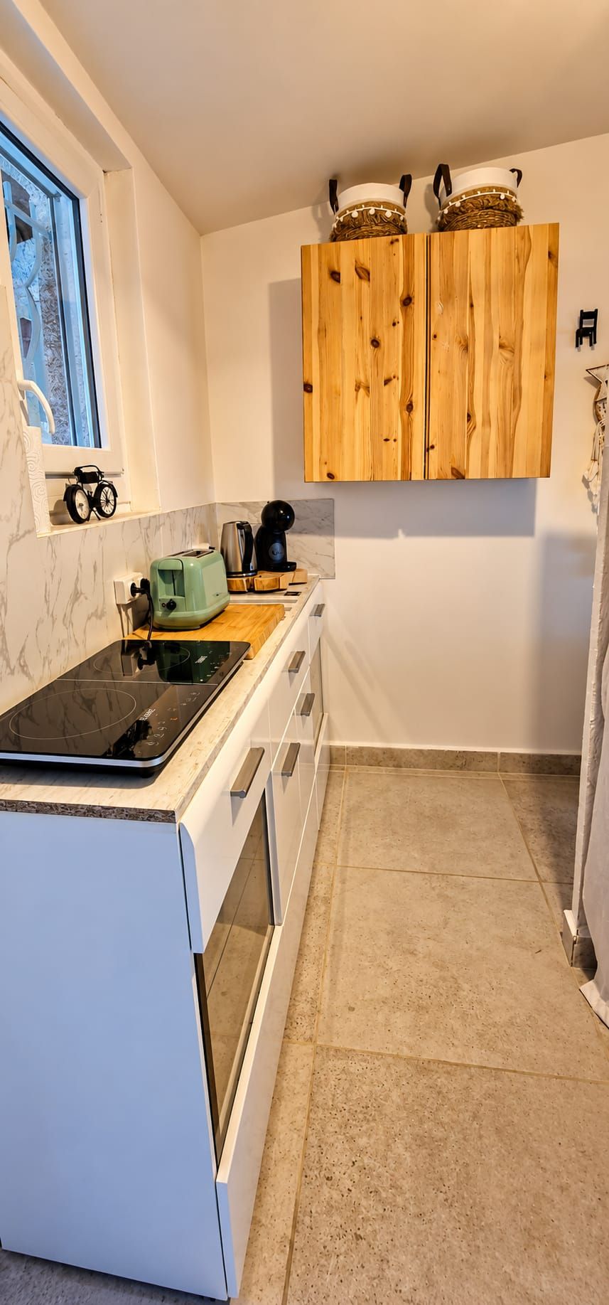 Une cuisine avec un four blanc, une plaque de cuisson à induction verte, des meubles en bois et une fenêtre donnant sur un beau paysage.