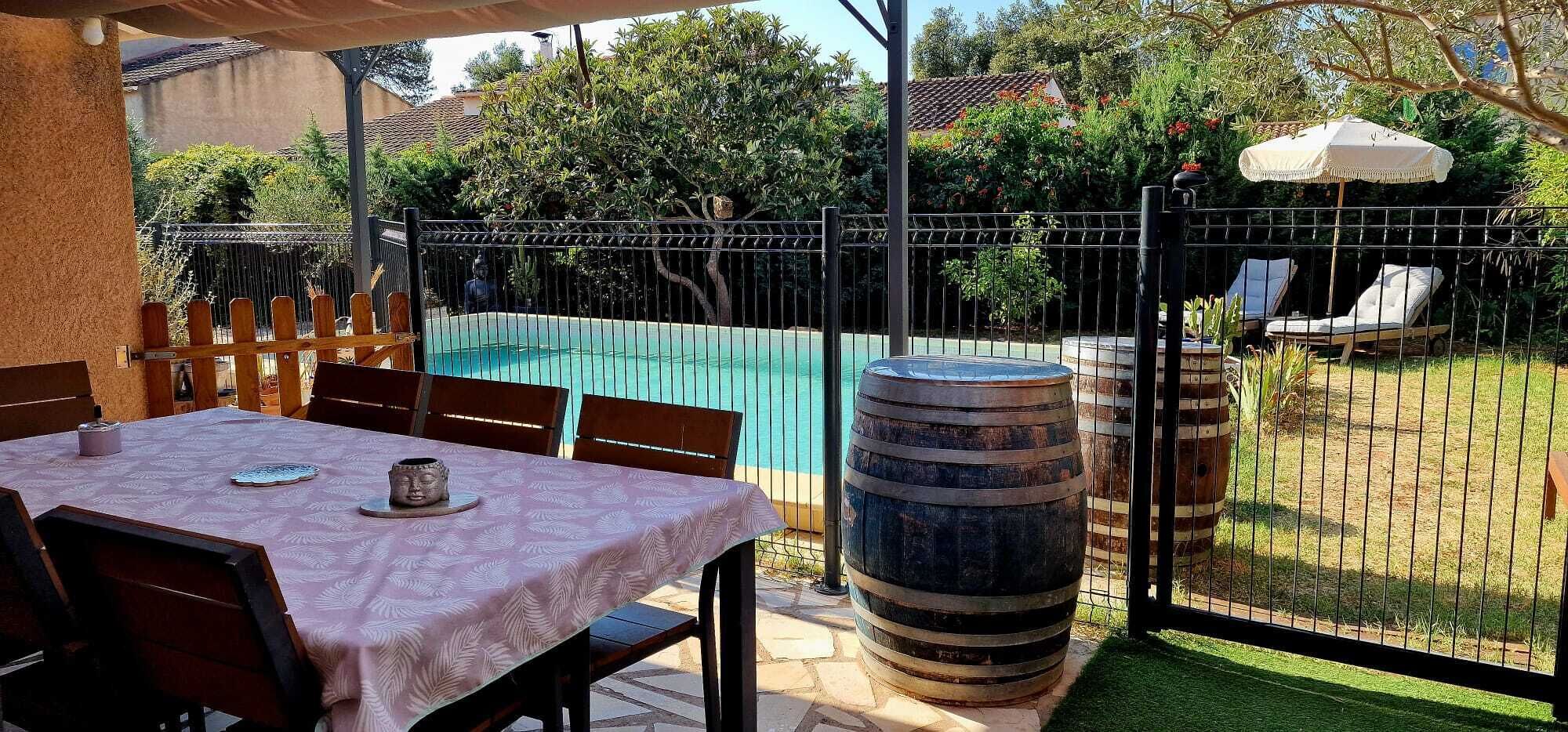 Eine Außenpatio mit Tisch und Stühlen, einem Metallzaun, einem großen Fass und einem Pool im Hintergrund.