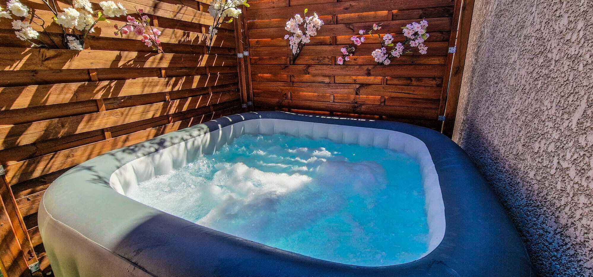 A hot tub in a wooden outdoor setting with a wooden wall and flowers.