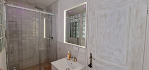 Un baño con cabina de ducha de vidrio, un lavabo blanco, un espejo y una puerta blanca.