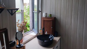 Ett litet badrum med ett fönster, ett handfat, en spegel och ett skåp.