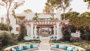 A modern outdoor seating area with a circular fire pit, stone walls, and a pergola structure. - Fully Staffed Seafront Villa Private Sommelier (Teulada)