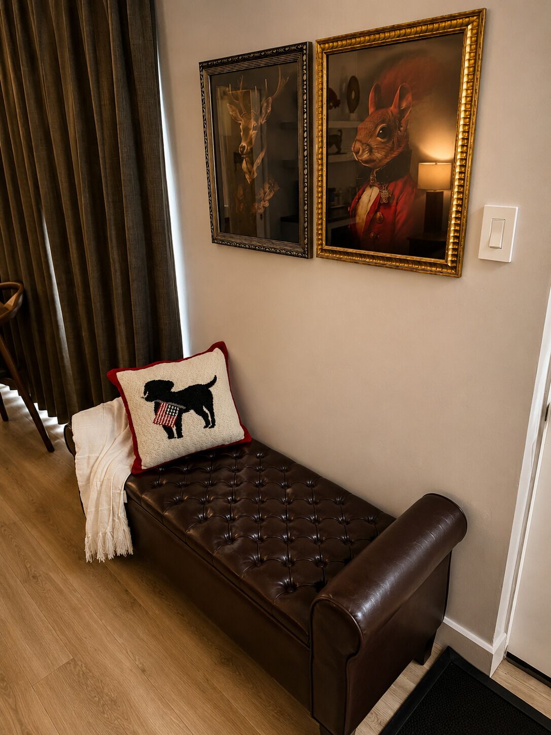 Ein Zimmer mit einer braunen Lederbank, einer weißen Tagesdecke, einem Kissen mit einer schwarzen Hundeumrisse und zwei gerahmten Bildern an der Wand.
