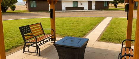 A covered patio area with a bench, a table, and a trash bin.
