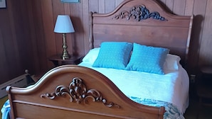 Uma cama de madeira com cabeceira, uma mesa de cabeceira com abajur e um cobertor estampado.